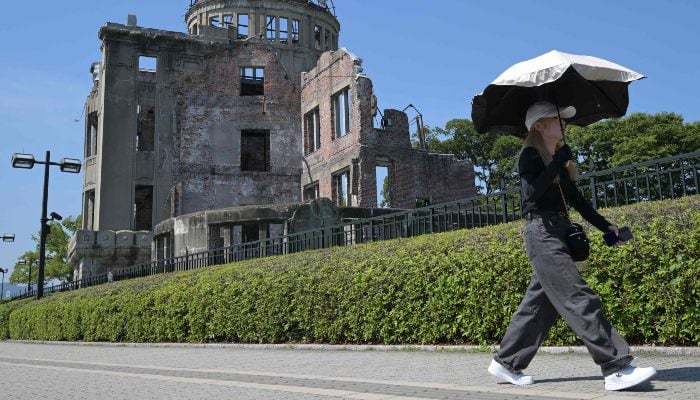 This photo taken on June 28, 2025 shows a woman using an umbrella to shield herself from the sun as she walks past the Atomic Bomb Dome in the centre of Hiroshima, Hiroshima prefecture, Japan. — AFP