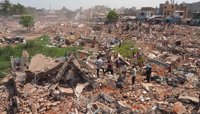 People stand amid the debris of a razed residential settlement who the authorities say belongs to illegal Bangladeshi nationals, near Chandola Lake in Ahmedabad on May 20, 2025. — AFP