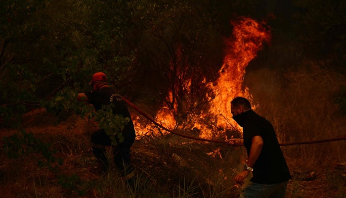 A firefighter (L) and a resident work to extinguish a wildfire near the city of Patras, western Greece on August 13, 2025. — AFP
