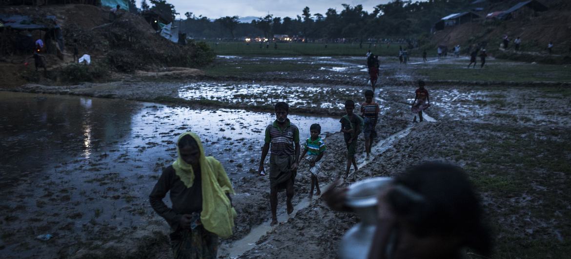Rohingya refugees walk across a muddy field in southern Bangladesh, as fires burn in a distance. (file photograph)