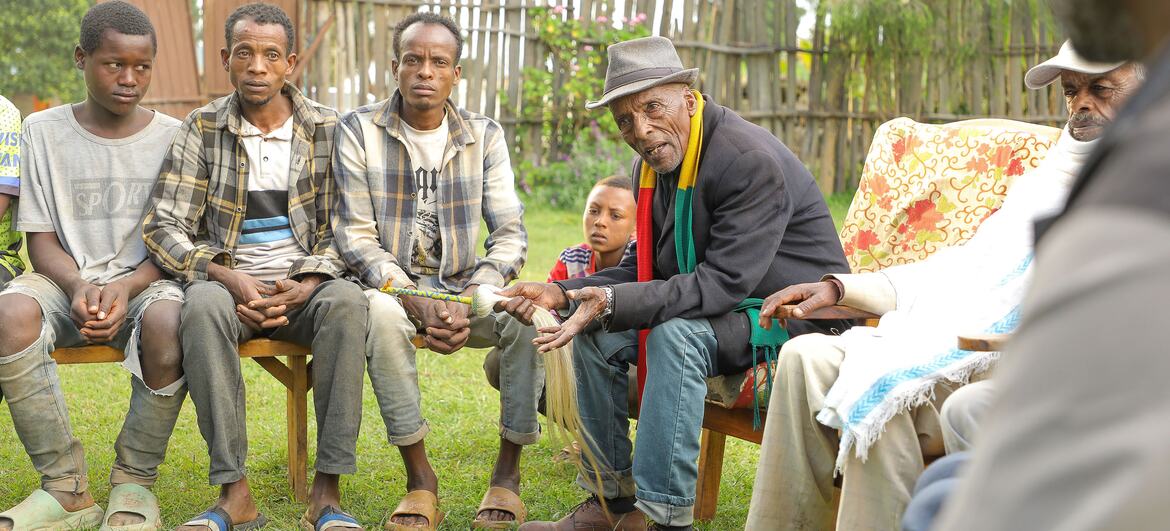 A group of men, including an older man speaking, sit together outdoors in a community setting, symbolizing resistance against female genital mutilation in Ethiopia.