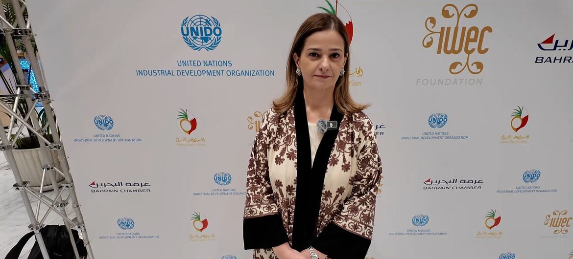 A woman in a patterned coat stands in front of a backdrop featuring UNIDO, Bahrain Chamber, and WEIF2026 logos at an event in Manama, Bahrain.