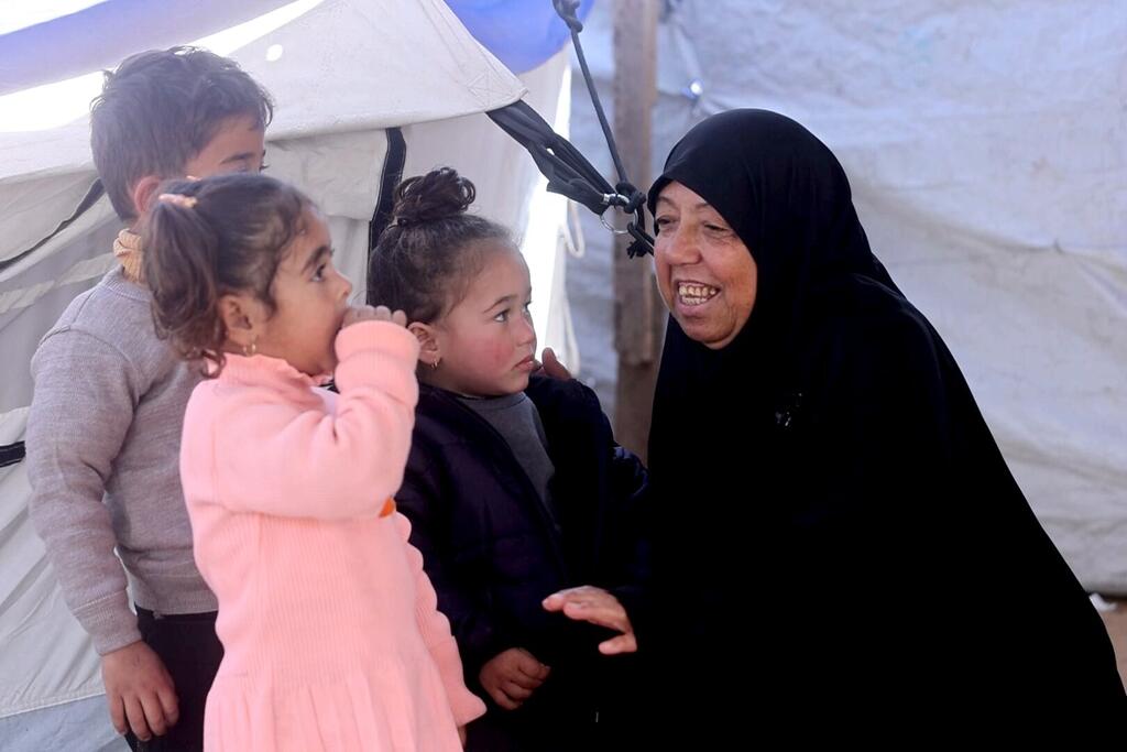 Amal Al-Samri, a mother, smiles with her children as they sit outside their tent beside a destroyed home in Gaza during Ramadan.